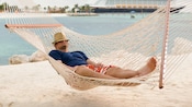 Um homem cochila em uma rede com um navio da Disney Cruise Line em segundo plano Um homem cochila em uma rede com um navio da Disney Cruise Line em segundo plano