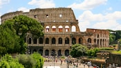 The ancient roman Colosseum stands tall on a sunny day above crowds of onlookers