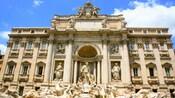 Statues of men wrangling horses in front of a large stone building with ornamental pillars