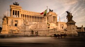 A statue of a winged figure stands before a multitiered structure adorned with engravings and pillars