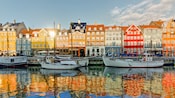 Buildings of similar heights sit side by side before a canal populated by sail boats