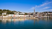 Cobh Harbor in Cork, featuring a serene marina, a row of houses and the Church of the Holy Rosary cathedral