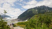 A small group of people look toward a glacier across a lake and bordered by mountains