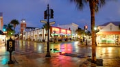 A public telephone, a streetlight and a palm tree on a street corner across from a bar