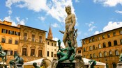 Una estatua de un hombre barbudo con una corona en una plataforma rodeada de otras estatuas sobre una fuente