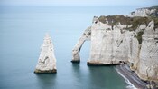 A large conical rock in a bay, next to a larger cliff with a gaping arch eroded into its side