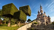 Hedge trees with box shaped branches lead up a hillside to a Disney castle