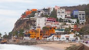 A coastline featuring a hill with buildings, palm trees, cars and pedestrians