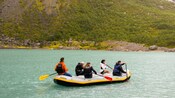 Five people paddling in an inflatable raft with a hillside in the background