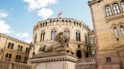 Statue of a lion sits infront of a circular building with the Norwiegan flag on its roof
