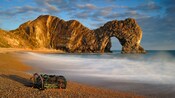 A beach featuring a shore covered with pebbles and shells, a large rock formation and more