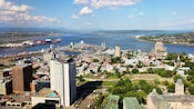 A city filled with trees, buildings and a crowded harbor near a populated body of water set against a backdrop of verdant hills