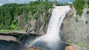 Spectators on a bridge look at a large waterfall surrounded by trees