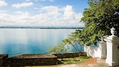 Wide shot of the ocean from atop a stone wall and walk way with trees