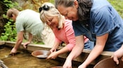 Two women smile while panning for gold in a trough