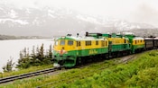 Locomotive travels along the coast line through mist with snow laced mountains in the background