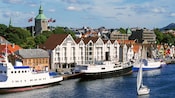 Ships moored in front of a row of builidings sitting side by side with pointed roofs