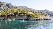 Boats near a rocky coastline with trees and a house
