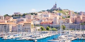 A marina full of boats near a city and a hill topped by a cathedral