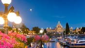 A marina filled with boats sits in front of a large building lined with lights with a domed roof