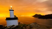 Un faro en un acantilado, con las luces de la ciudad de Vigo, España, bordeando la costa en el fondo