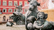 Fountain statue of a bull with hooves raised behind a another statute of a woman holding a baby