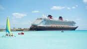 A Disney Cruise Line ship near an island, a catamaran and people swimming in the ocean