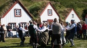 Folk dancers performing amid turf houses outside