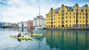2 kayakers paddle the calm waters of a canal lined with gabled buildings