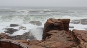 A frothing sea smashes up against rocks with stairs that descend into the spray