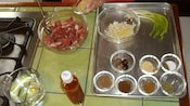 Ingredients for cooking, including meat, onions and spices are in separate bowls on a kitchen counter