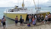 Guests pause on the sand next to a partially beached catamaran
