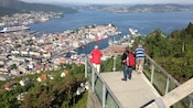 Três turistas veem a cidade de Bergen e seu porto de um mirante na encosta