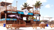 Un bar de dos pisos en una playa cerca de mesas de pícnic y palmeras
