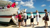 A group of people on a beach board a ferry with a sign that reads Kantika Too