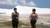 Two women ride Segways in front of salt mounds