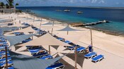 Camastros y toldos en una playa cerca de un muelle y barcos