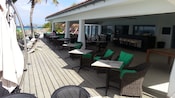 A restaurant seating area with chairs, tables, an overhang and parasols near a beach