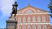 A statue of Samuel Adams with the inscription 1722 through 1803 stands in front of a brick building