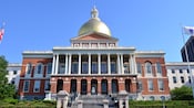 A brick building featuring windows, columns, outdoor statues and a high dome