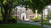 Tables with umbrellas front a formidable red-brick building with an abundance of trees
