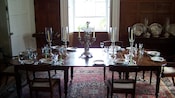 A dining table with 6 chairs is set with a candelabra, fine dishes, glasses and flatware