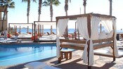 Canopy beds sit next to a pool at a beach side hotel resort