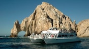 A catamaran filled with passengers cruising alongside the El Arco rock formation in Cabo San Lucas