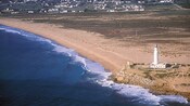 A sandy shoreline with a rocky outcropping where a lighthouse sits atop