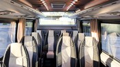 El interior de un minibús con asientos cómodos, cortinas en las ventanas y abundante espacio para guardar equipaje