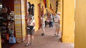 People shop at a brightly colored row of shops with a brick walkway