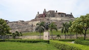 A statue in front of a large stone fortress near trees and bushes