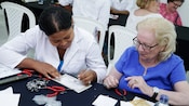 Una mujer firma un certificado cerca de las herramientas para hacer joyas y de otra mujer