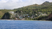 A boat sailing by a shoreline with houses crowding a grassy hillside